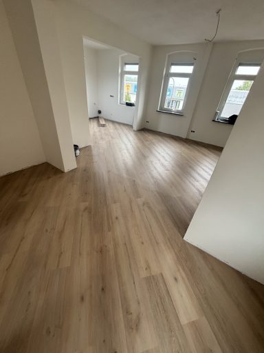 Helle, leere Raum mit neu verlegtem Holzfußboden und Fensterlicht.