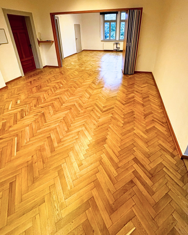 Holzboden in einem hellen Raum mit offenen Türen und Fenstern.