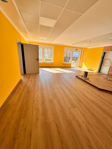 Heller Raum mit orangefarbenen Wänden und Holzfußboden, große Fenster und eine Tür.