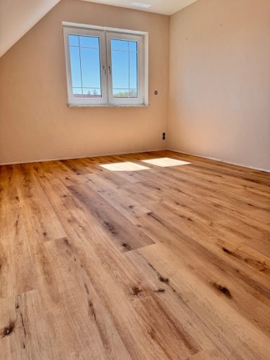 Heller Raum mit Holzfußboden und Fenster im Dachgeschoss.
