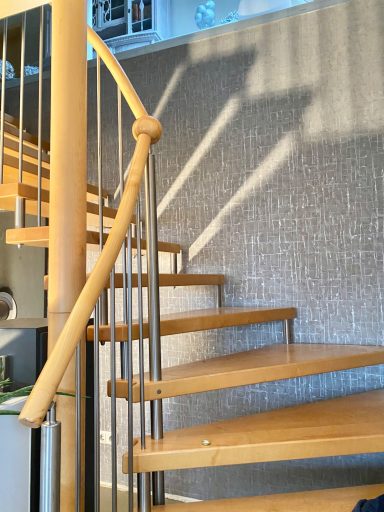 Holzspiraltreppe mit metallischen Geländern und Schatten an der Wand.