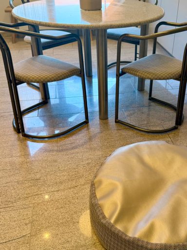 Runder Tisch mit zwei Stühlen und einem Hocker auf einem hellen Boden.