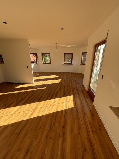 Heller Raum mit Holzfußboden und mehreren Fenstern, die für Tageslicht sorgen.