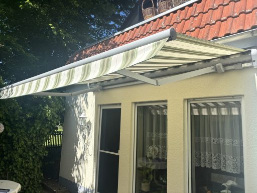 Markise in grünen Streifen über einem Fensterausschnitt eines Hauses.