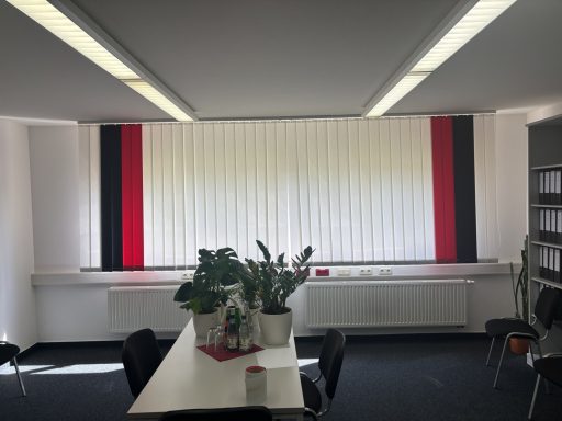 Büro mit weißen Jalousien und roten sowie schwarzen Akzenten, Pflanzen auf dem Tisch.
