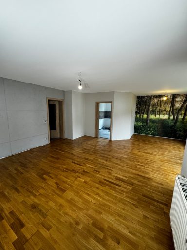 Heller Raum mit Parkettboden und Blick auf einen grünen Außenbereich.