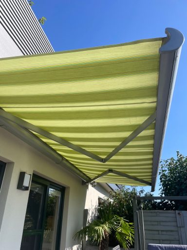 Grüne Markise über einer Terrasse vor einem klaren blauen Himmel.
