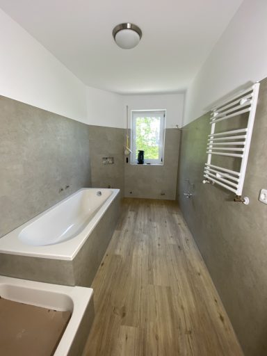 Heller Badezimmer mit Badewanne, Fenster und Heizkörper an der Wand.