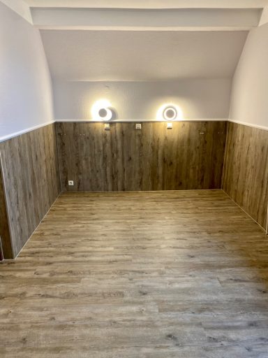 Helle, leere Raum mit Holzverkleidung und zwei Wandleuchten.