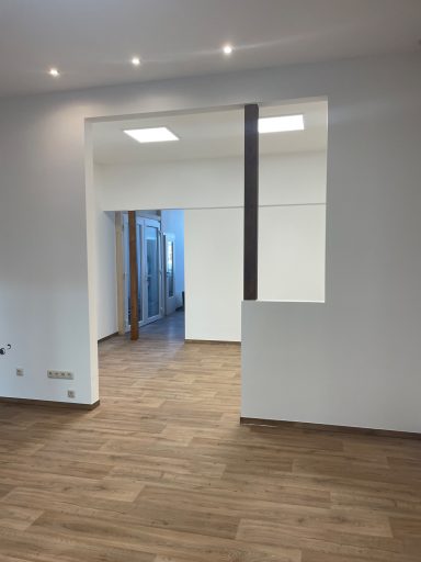 Heller, moderner Raum mit Holzfußboden und offener Durchgang zu einem weiteren Bereich.